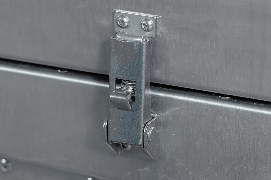 Închizătoare metalică gri pe o valiză argintie, cu finisaj lucios și nituri.